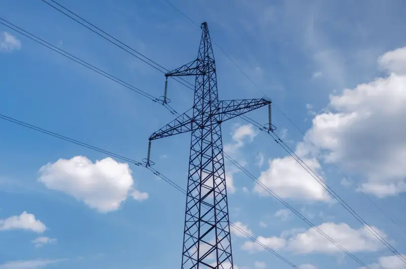 High-voltage transmission tower carrying lines against a blue sky with white clouds