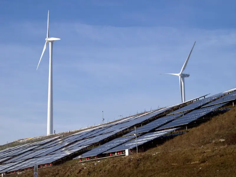 Two wind turbines above solar panels on a grassy hillside