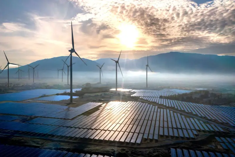 Wind turbines and solar arrays in morning mist with mountains behind