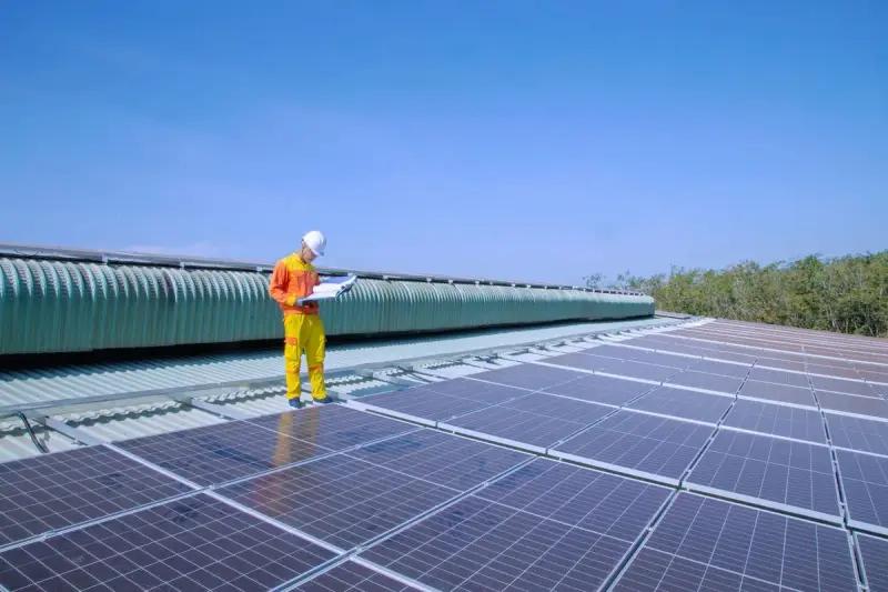 Solar technician inspecting newly installed panels under a clear blue sky