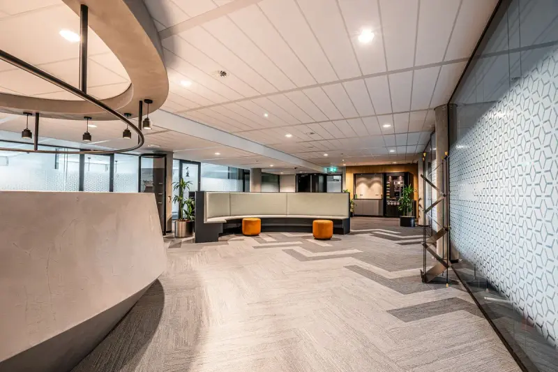 Modern office reception with a curved desk, lounge sofas and patterned carpet under a sculpted ceiling