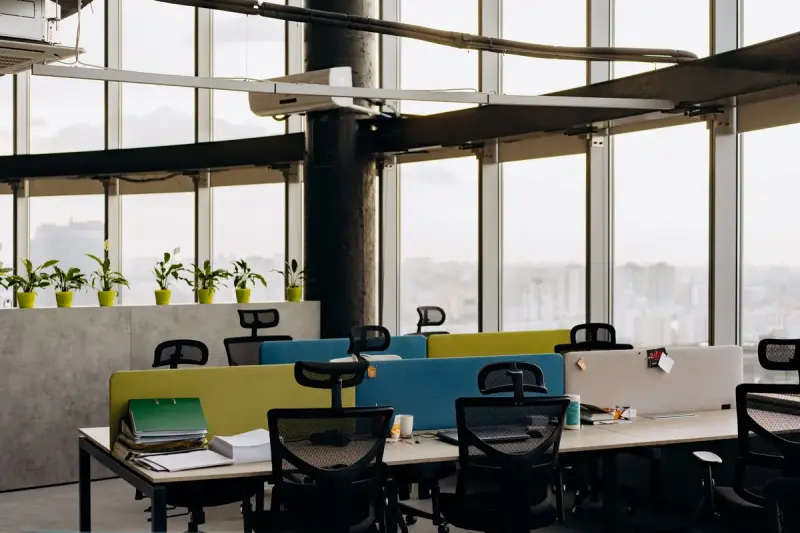 Open office of desks with colorful dividers and tall windows over a city view