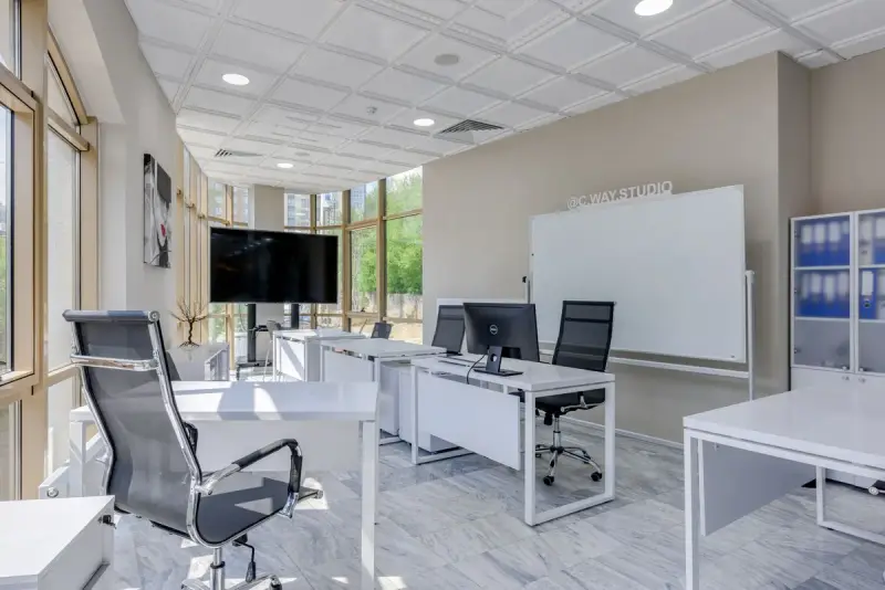 Bright office with white desks, mesh chairs, a wall screen and floor-to-ceiling glazing