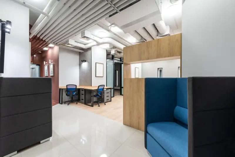 Office corner with a high-back blue lounge booth, wood paneling and acoustic ceiling baffles