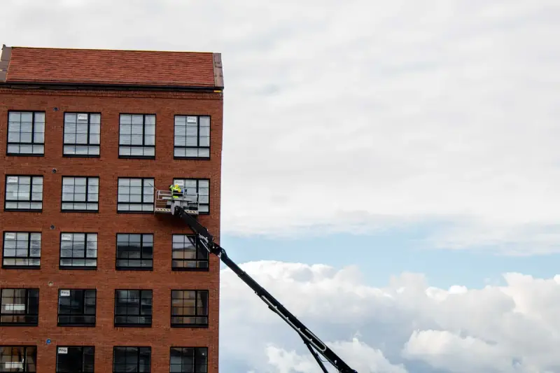 Worker on a telescopic lift platform inspecting the upper windows of a red brick building