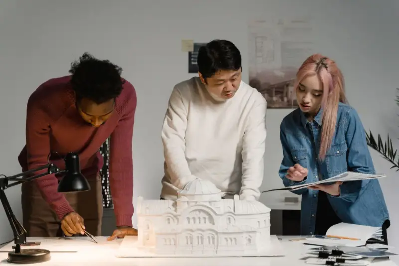 Three colleagues leaning over a white architectural model, marking notes on a drawing