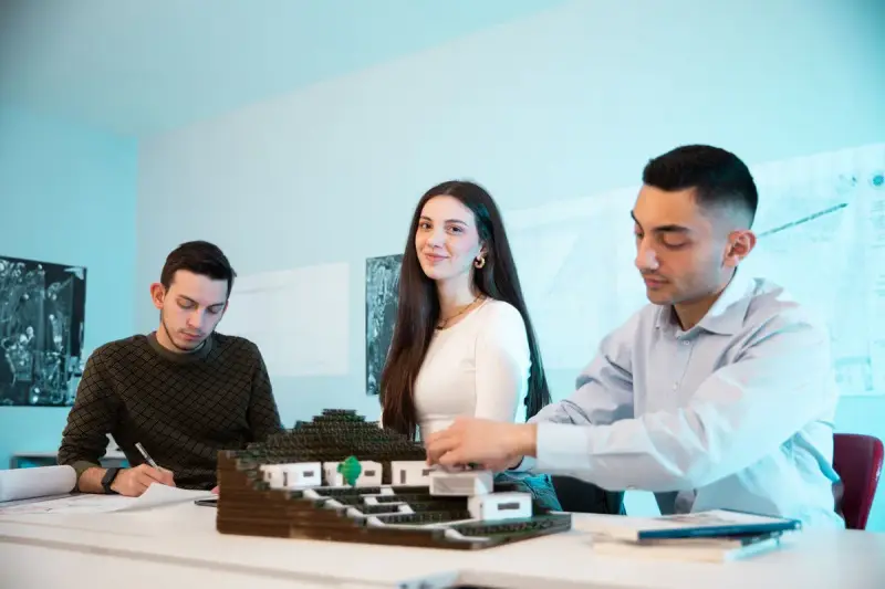 Three young professionals at a table with a site model and drawings in a bright office