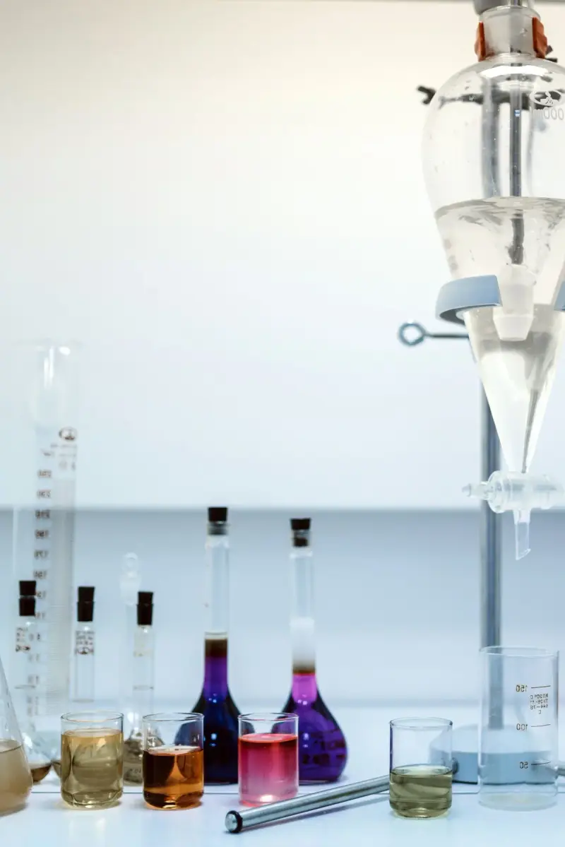 Volumetric flasks with colored liquids and a separating funnel on a white lab bench