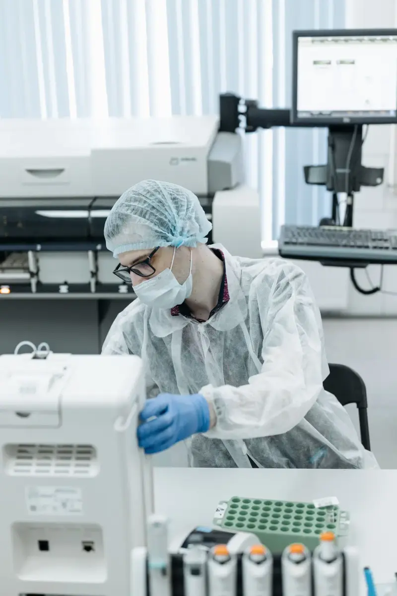 Scientist in a hairnet, mask and gown loading samples into an automated instrument