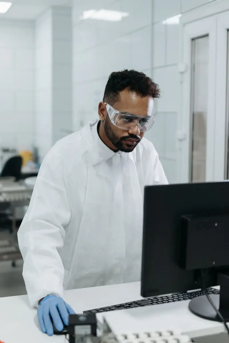 Scientist in safety glasses and gloves working at a lab computer