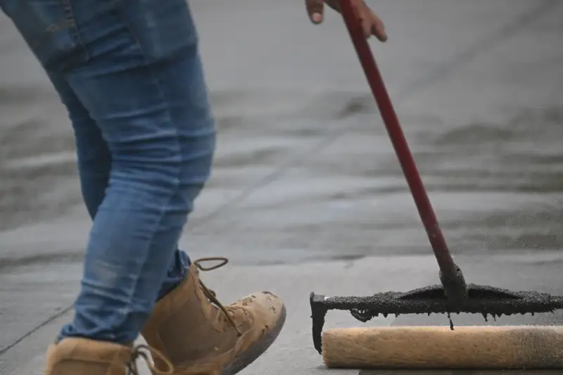 Worker in boots rolling liquid sealant across a concrete surface