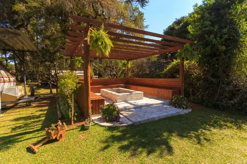 Wooden pergola over a stone patio with raised planters in a sunny backyard