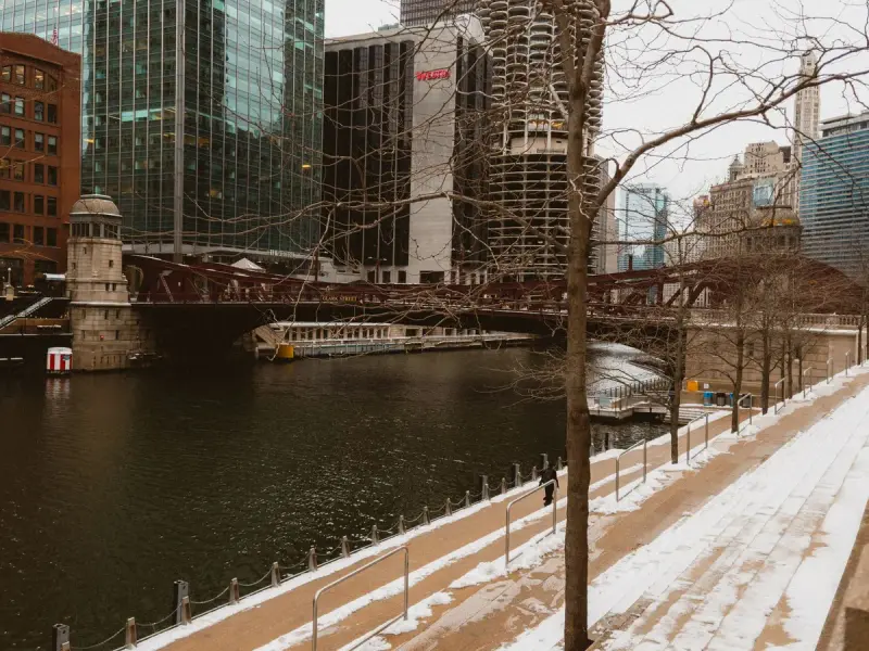 Snow-dusted Chicago Riverwalk with a historic bridge and downtown towers