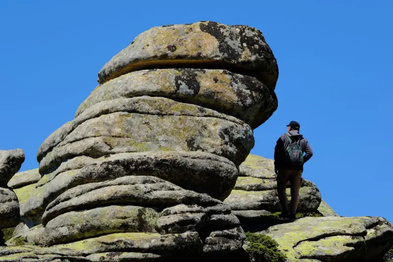 Person with a backpack studying a layered rock formation under a clear blue sky