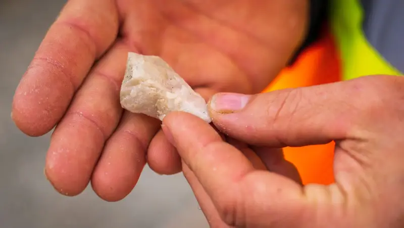 Hands holding and examining a white mineral specimen outdoors
