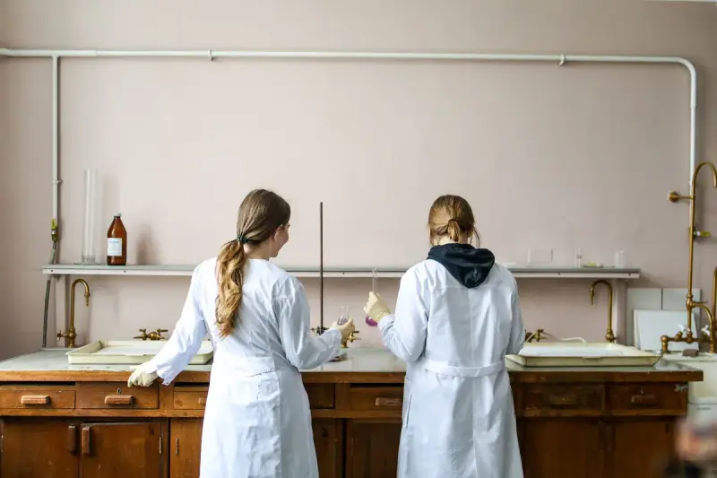Two researchers in white lab coats working side by side at a long wooden lab bench
