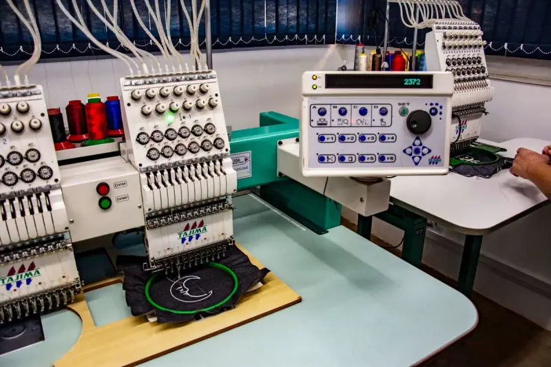 Multi-head industrial embroidery machines with colorful thread cones in a textile workshop