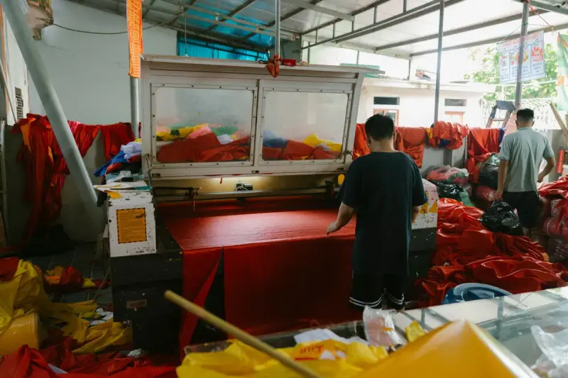 Workers running machines in a busy textile workshop full of red and yellow fabric
