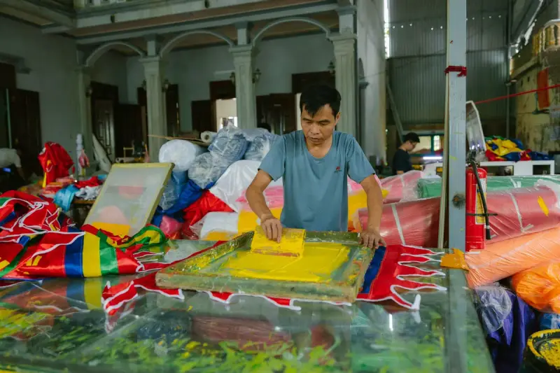 Printer pulling ink through a screen on a long table piled with colorful printed fabric