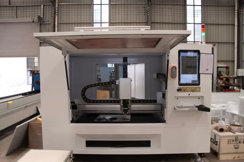 Open CNC fiber laser cell standing in a bright factory hall beside other machines