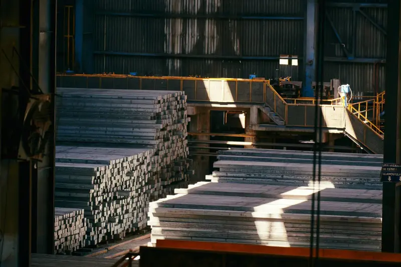 Stacks of steel bar stock catching shafts of sunlight inside a large metals hall