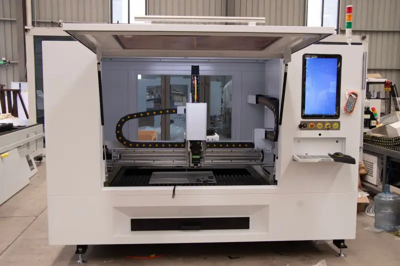 Enclosed CNC laser cutting cell with its door raised, gantry head and touchscreen control