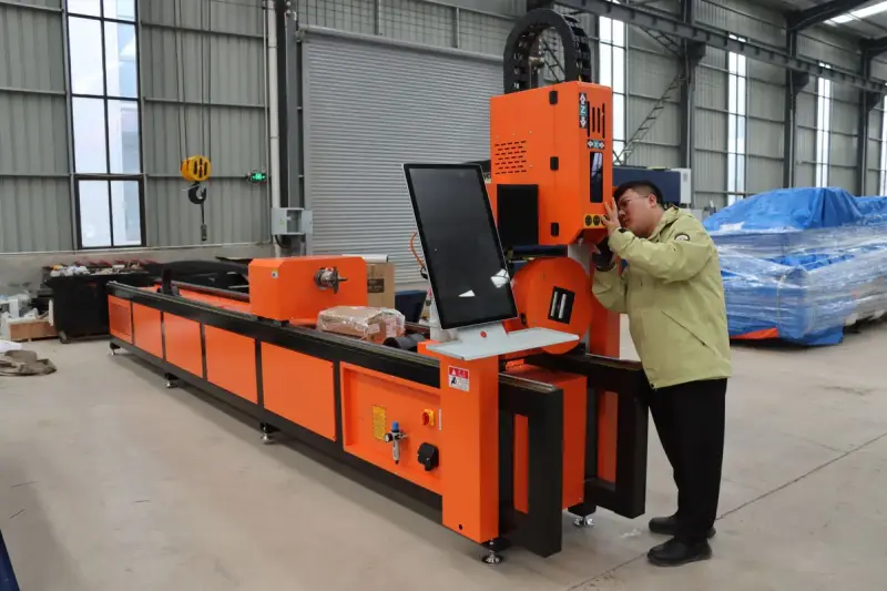 Technician leaning in to adjust an orange CNC tube cutting machine in a factory hall