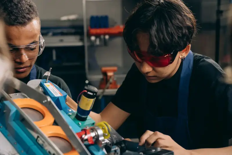 Two young engineers in safety glasses concentrating on precision work at a machine