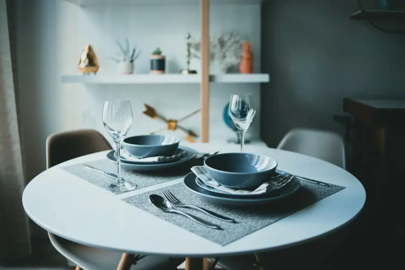Round white dining table set for two with blue bowls, stemware and cutlery