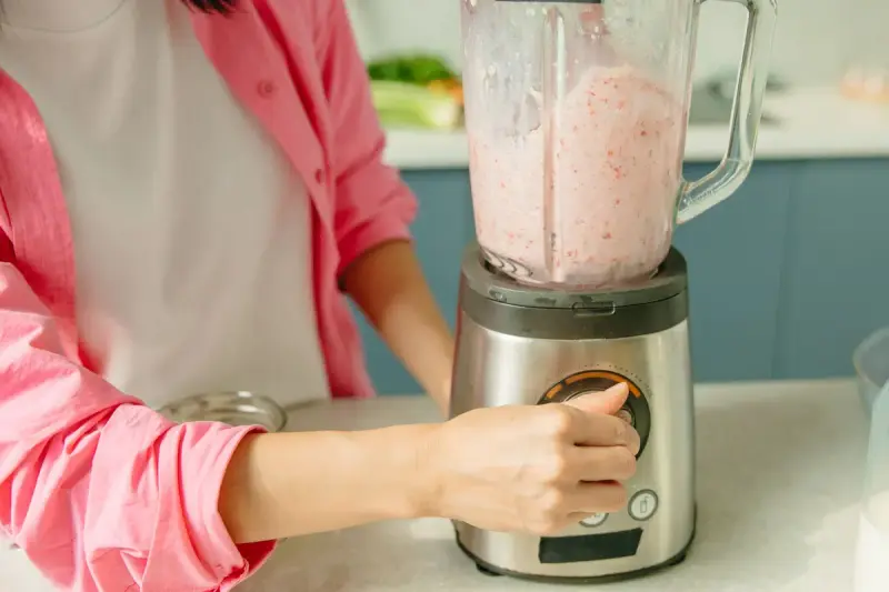Hand turning the dial of a countertop blender full of a pink fruit smoothie