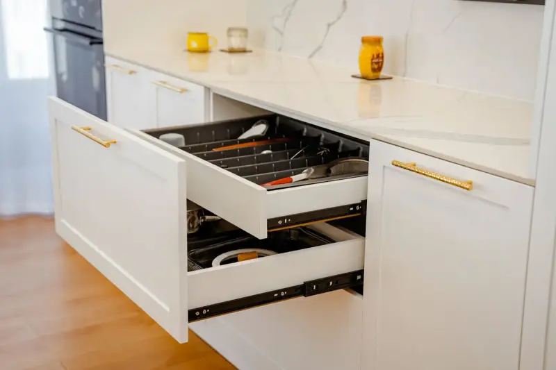 Open white kitchen drawers with organized utensil dividers below a marble counter