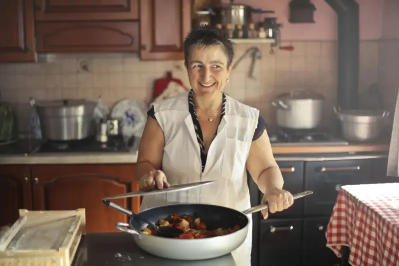 Smiling woman in an apron cooking with a frying pan in a rustic home kitchen