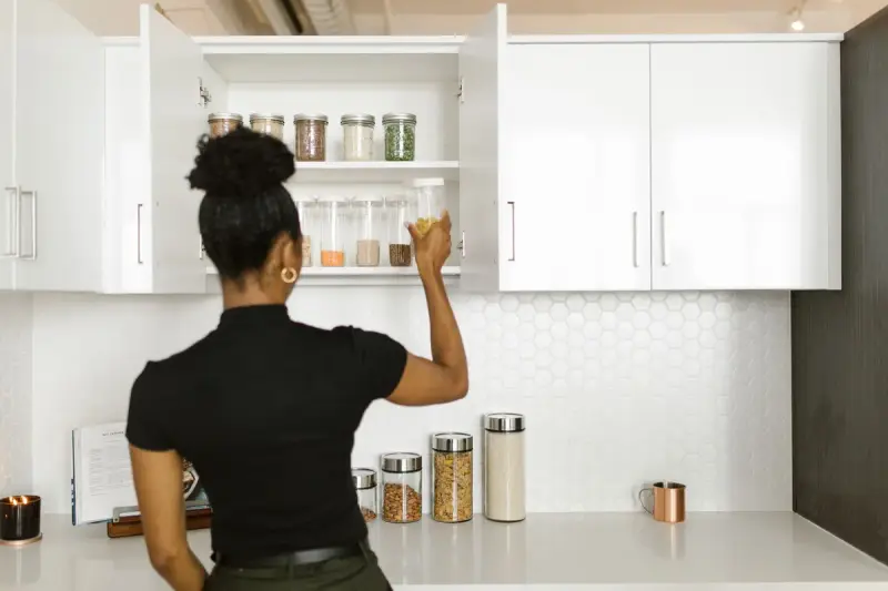 Woman placing glass storage jars onto an open shelf in a white kitchen cabinet