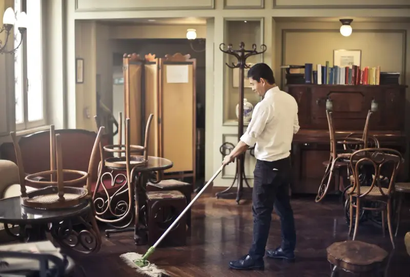 Man in a white shirt mopping the wooden floor of a vintage cafe dining room