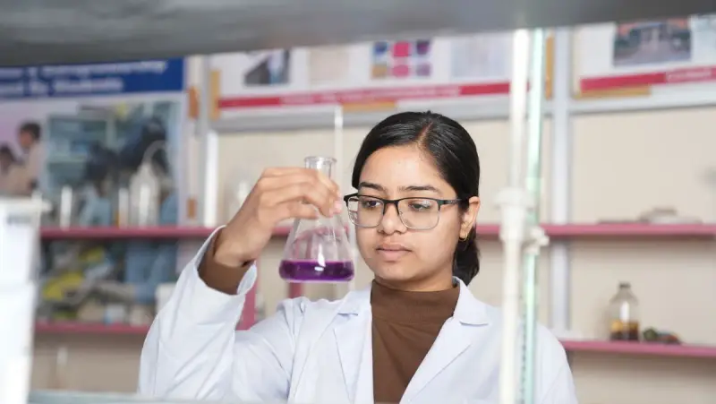 A female scientist in a lab coat examines a purple chemical solution in a flask