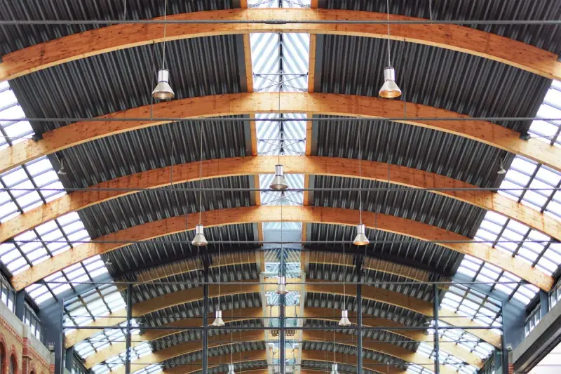 Curved glulam arches span a long glazed hall roof with pendant lights hanging between them
