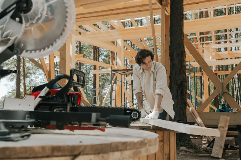Carpenter working with tools on a wooden frame at an outdoor site