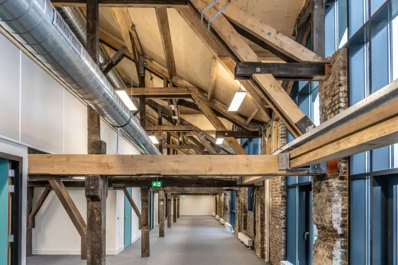 Corridor under exposed heavy timber roof trusses with ductwork and tall windows