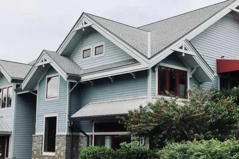 Blue lap-sided house with grey asphalt shingle gables, white trim and a standing-seam metal awning