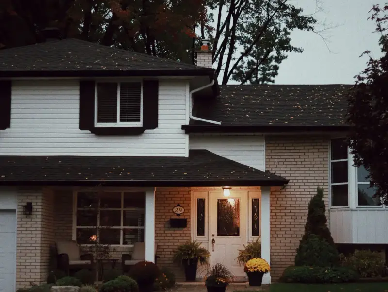 Two-story brick and siding house with dark shingle roof and gutters at dusk