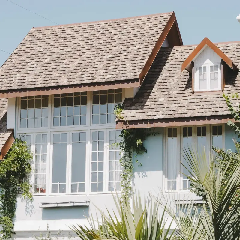 Light blue house with steep shingle roofs, a dormer and tall white-framed windows