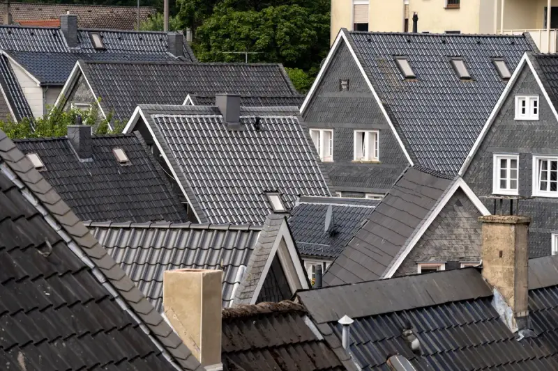 Rows of dark grey tiled and slate roofs with dormers and chimneys in a dense neighborhood