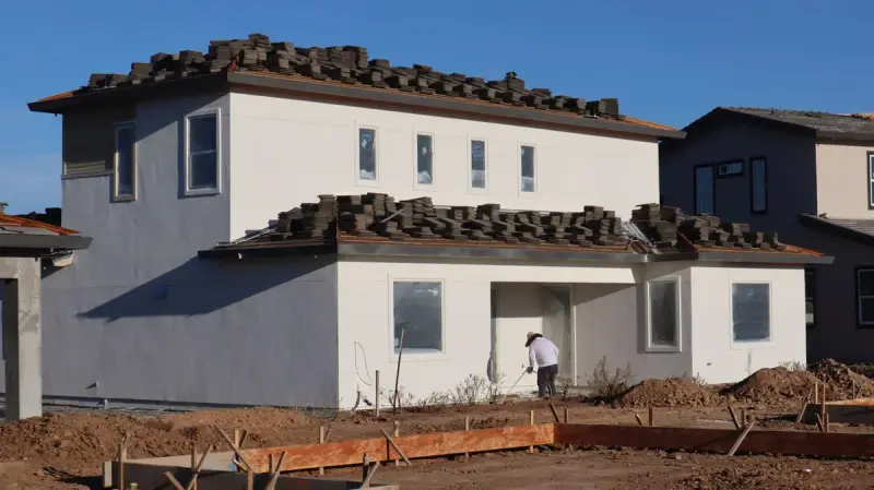 New two-story stucco house with roof tiles stacked on the roof and a worker at the front
