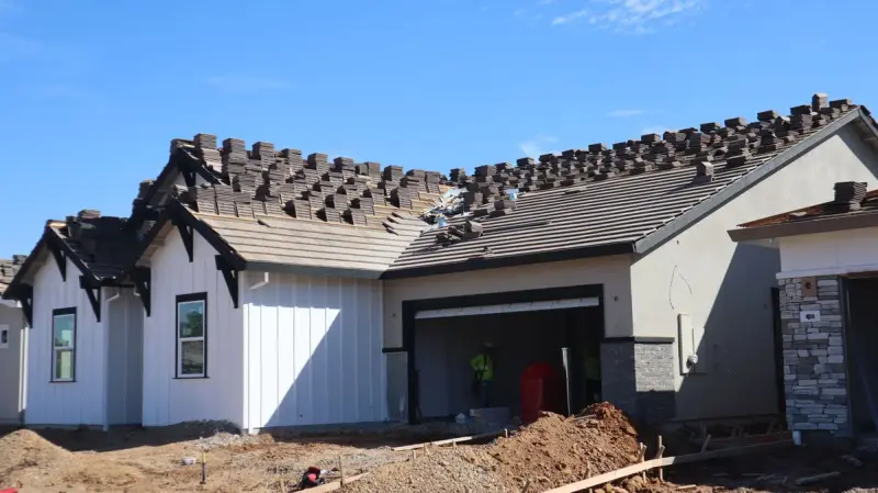 Workers in safety vests at a new single-story home with concrete tiles being laid on the roof