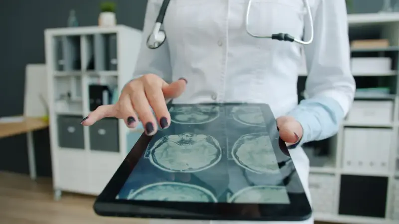 A woman doctor reviewing digital brain scans on a tablet in a medical office