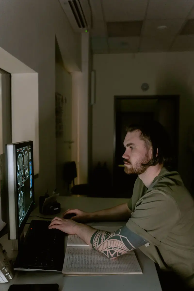Radiologist in scrubs reading brain scans on a monitor in a dim reading room