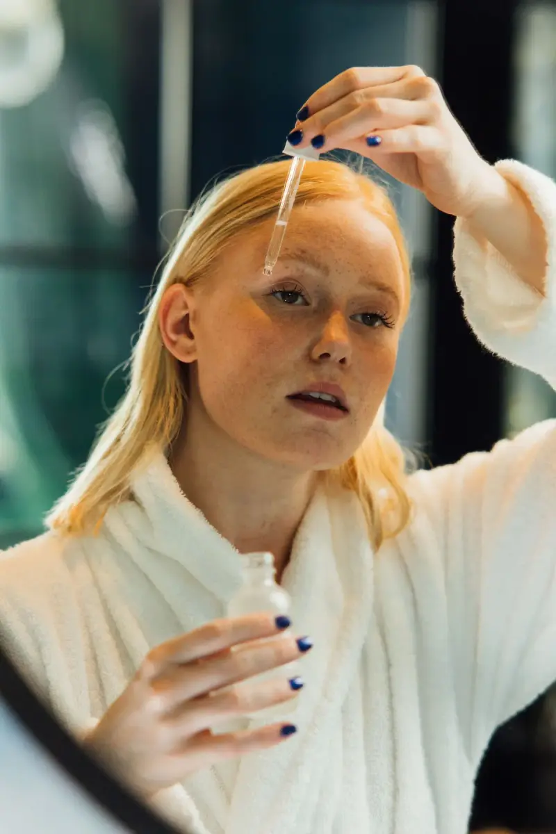 Woman in a white robe applying face oil with a dropper
