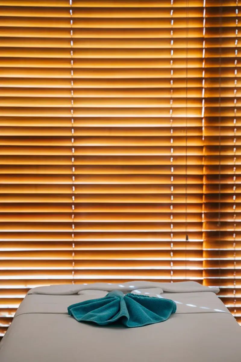 Massage table with a folded teal towel in front of wooden blinds