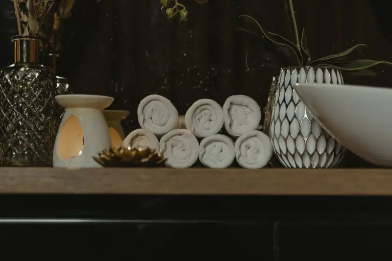 Rolled spa towels, candles and vases on a wooden shelf