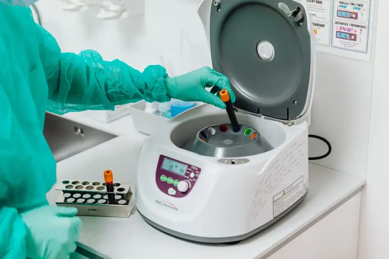Gowned and gloved hand loading a tube into an open benchtop centrifuge